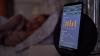 A person sleeps on a bed next to a sleep tracker app on their phone, which is displaying data.