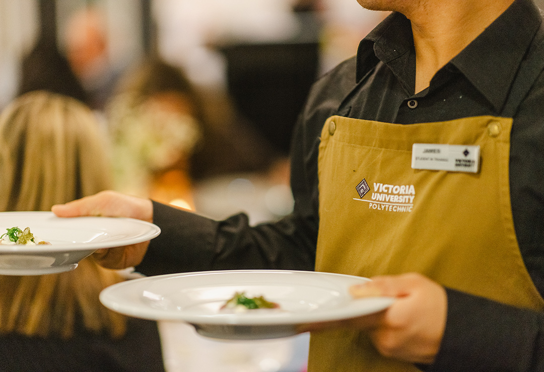 Wait staff in a Victoria University apron carries sophisticated looking dish