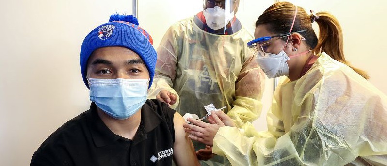 Young man getting a vaccination in a Western Bulldogs beanie and surgical mask