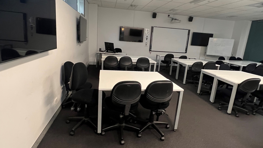  Two rows each with three desks and surrounded by computer chairs. Towards the back of the room is a digital whiteboard and desk.